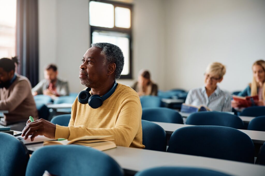 Black senior man paying attention during adult educational training class in lecture hall.