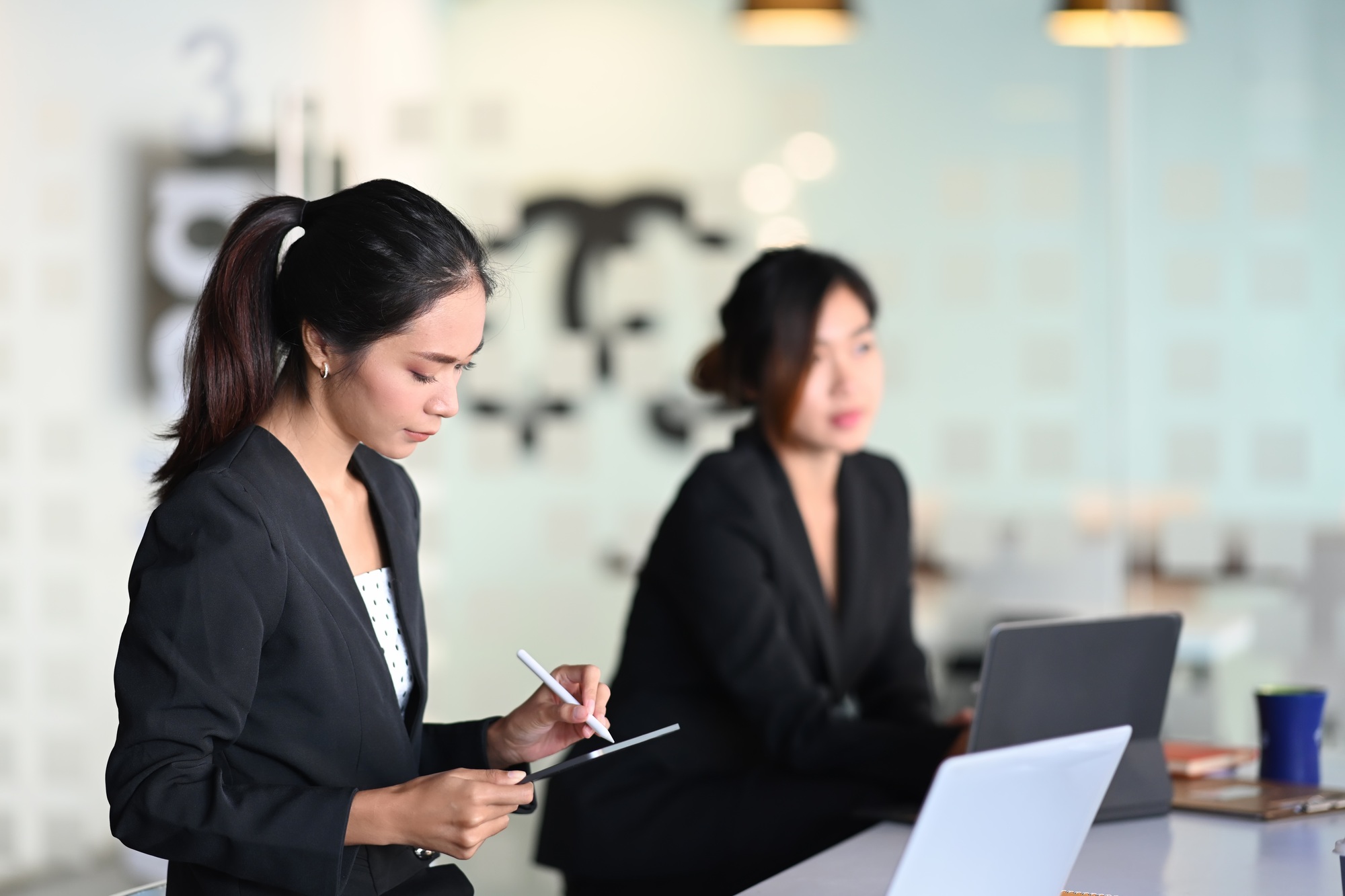 Businesswoman sitting in office with her colleague and writing business plan on notebook.